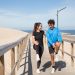 A young couple doing warm-up exercises on a boardwalk by the beach, enjoying a healthy lifestyle outdoors.